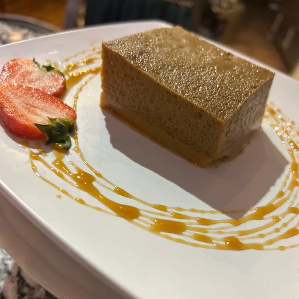 Watalappan, a Sri Lankan coconut custard, with sliced strawberries and caramel drizzle on a white plate.