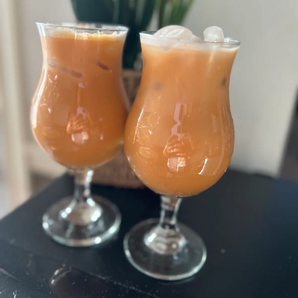 Two glasses of iced orange drinks with foam, possibly Sri Lankan faluda, on a dark table.