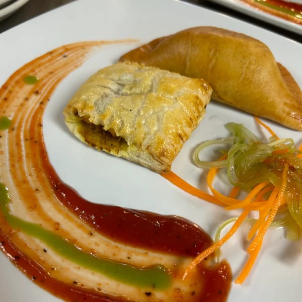 Two golden-brown Sri Lankan pastries, one square and one crescent, with colorful sauces and pickled vegetables.