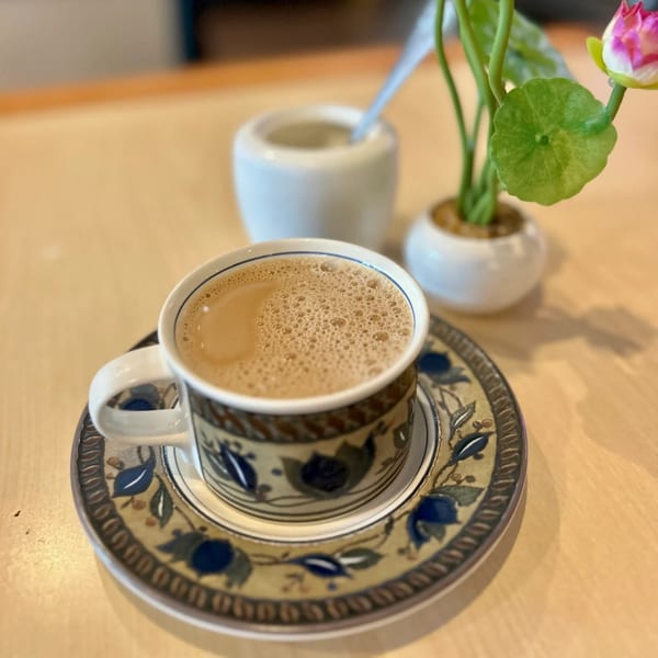 A cup of Sri Lankan milk tea with foam, sugar pot, and a small plant on a wooden table.