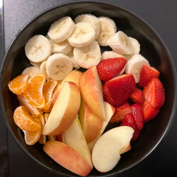 A black bowl filled with sliced bananas, strawberries, tangerine segments, and apple wedges.