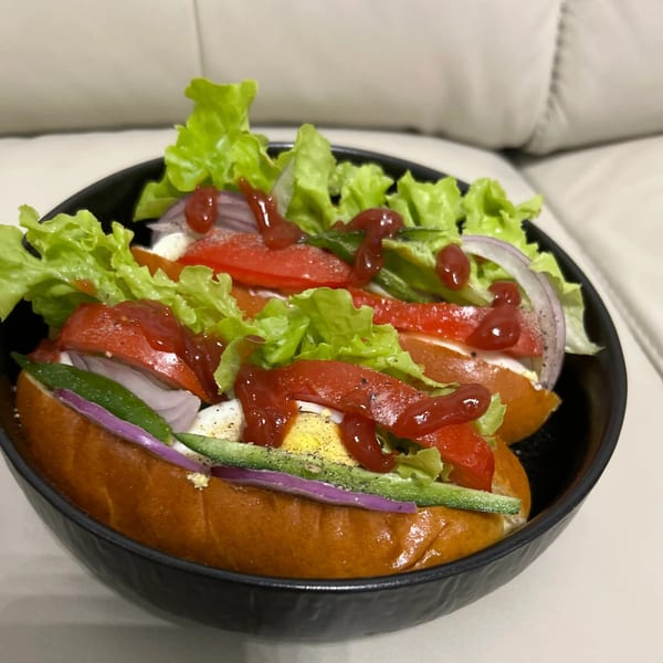 Two Sri Lankan style hot dogs with lettuce, tomato, onion, egg, and ketchup in a black bowl.
