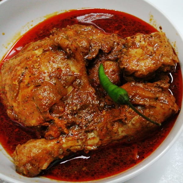 Spicy Zest's Sri Lankan chicken curry, rich red sauce, and a green chili in a white bowl.
