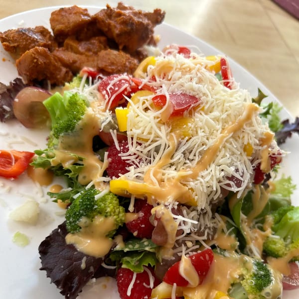A plate of Sri Lankan chicken curry with a fresh salad topped with cheese and dressing.