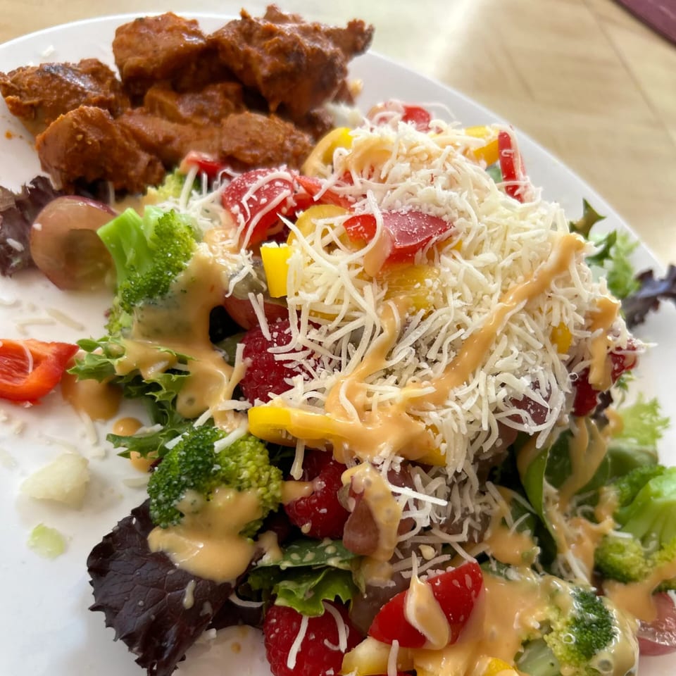 A plate of Sri Lankan chicken curry with a fresh salad topped with cheese and dressing.